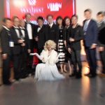 Group of people posing for a picture with an entertainer disguised as Marylin Monroe.
