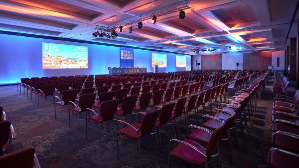 Big conference room with several rows of chairs in front of a wall with LED screens and projections.