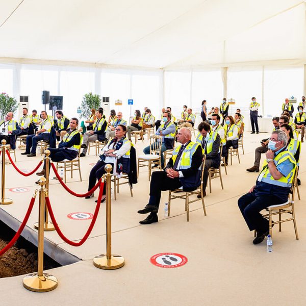 Group of people wearing masks, listening to a speaker talking during an event inside a tent.
